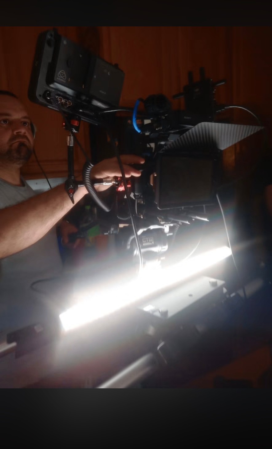 Camera operator lit by a tube light while framing a shot in a dark room